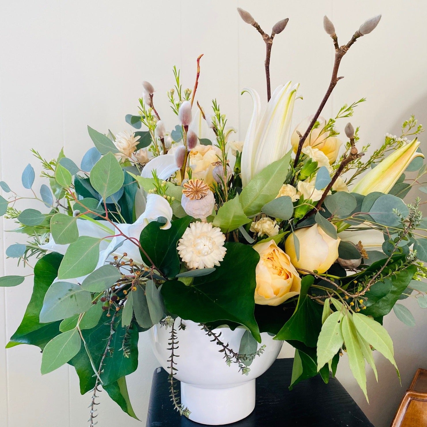 soft yellows and white flowers with mixed seasonal greenery in white ceramic vase