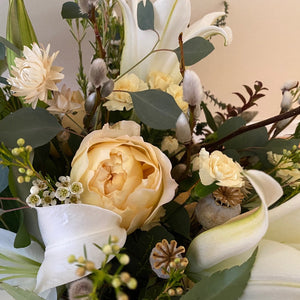 soft yellows and white flowers with mixed seasonal greenery in white ceramic vase
