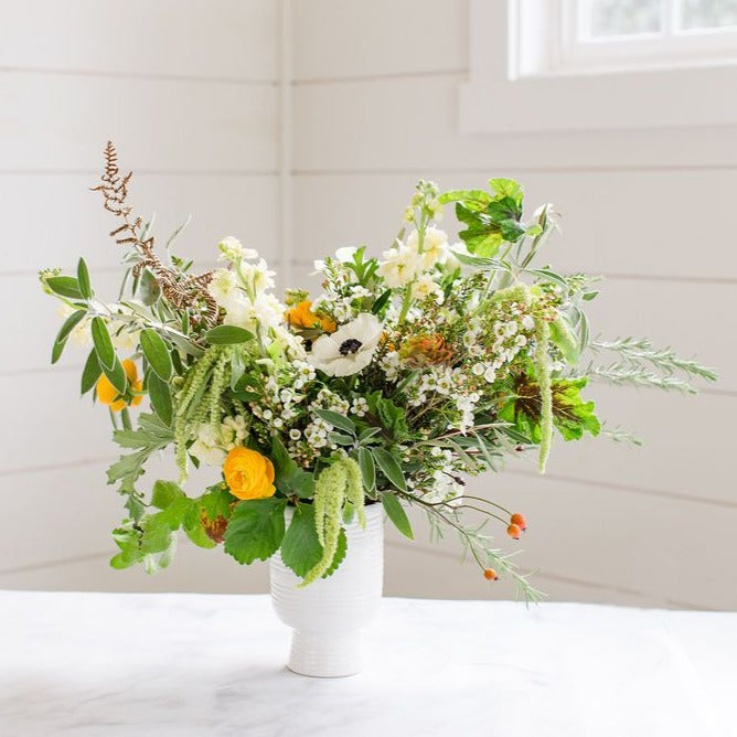 white and yellow flowers with mixed greenery in white ceramic vase